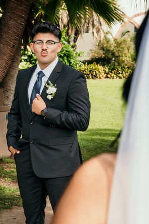 Groom in black suit with boutonniere makes funny face during first look at outdoor wedding ceremony.