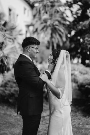 Black and white photo of bride and groom sharing a tender moment outdoors with palm trees in background.