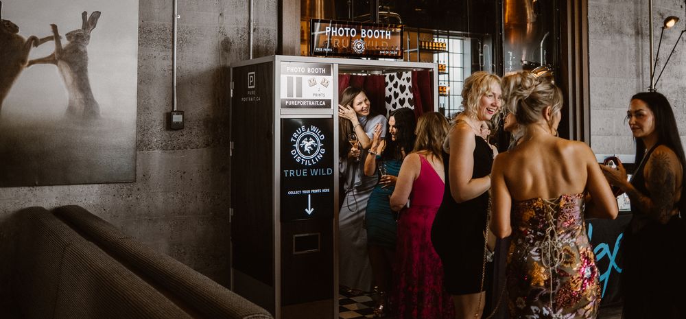 Guests gather around a photo booth at an elegant indoor event venue during a lively party or wedding reception.