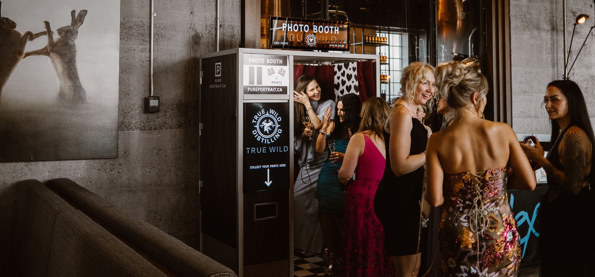 Guests gather around a photo booth at an elegant indoor event venue during a lively party or wedding reception.