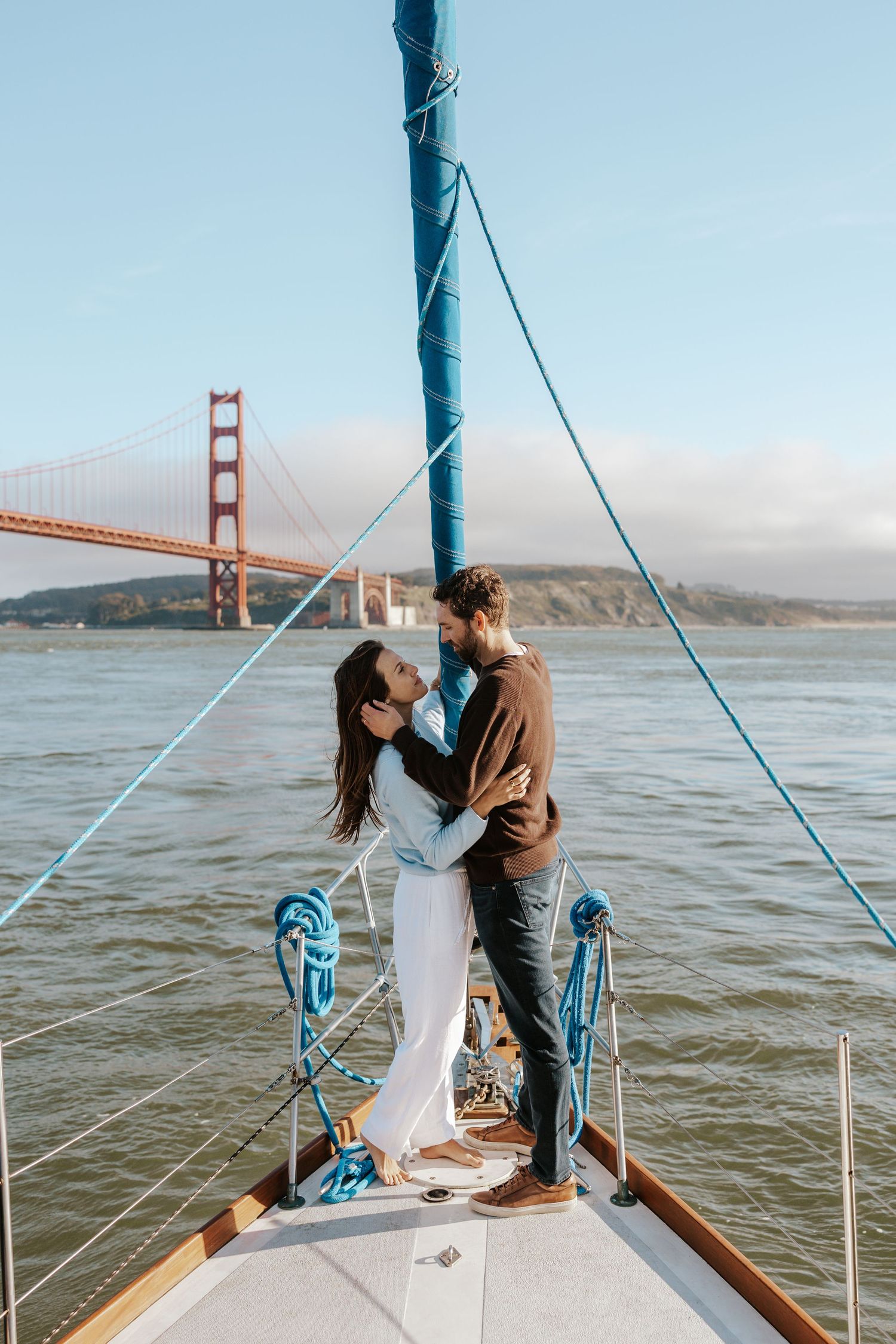 couple staring into each other's eyes on bow of sailboat in the SF bay with the golden gate bridge behind them