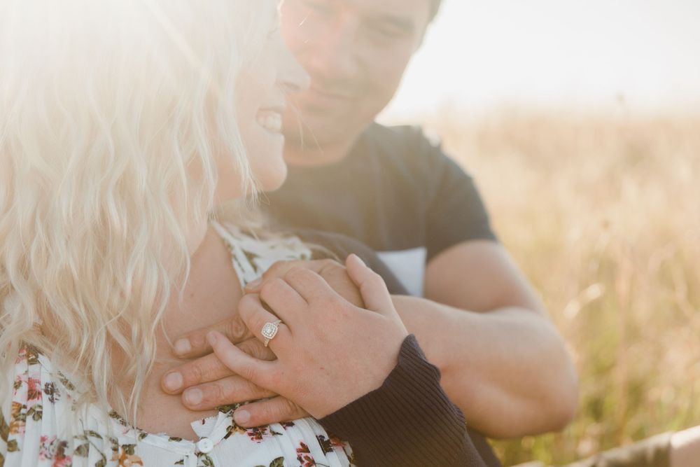 close up of a Newly engaged couple sitting cuddling during goldenhour showing the engagement ring