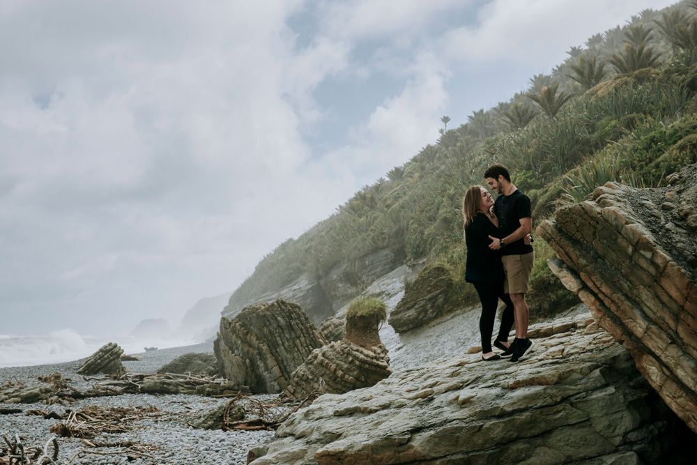 Couple standing on rocks cuddling on a West Coast beach.