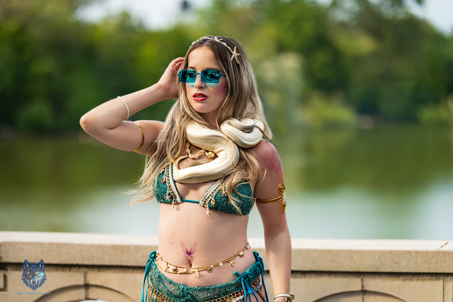 Woman in teal belly dancer cosplay with gold snake and sunglasses poses outdoors near water. Chi.Shooters meet @madisoneliac