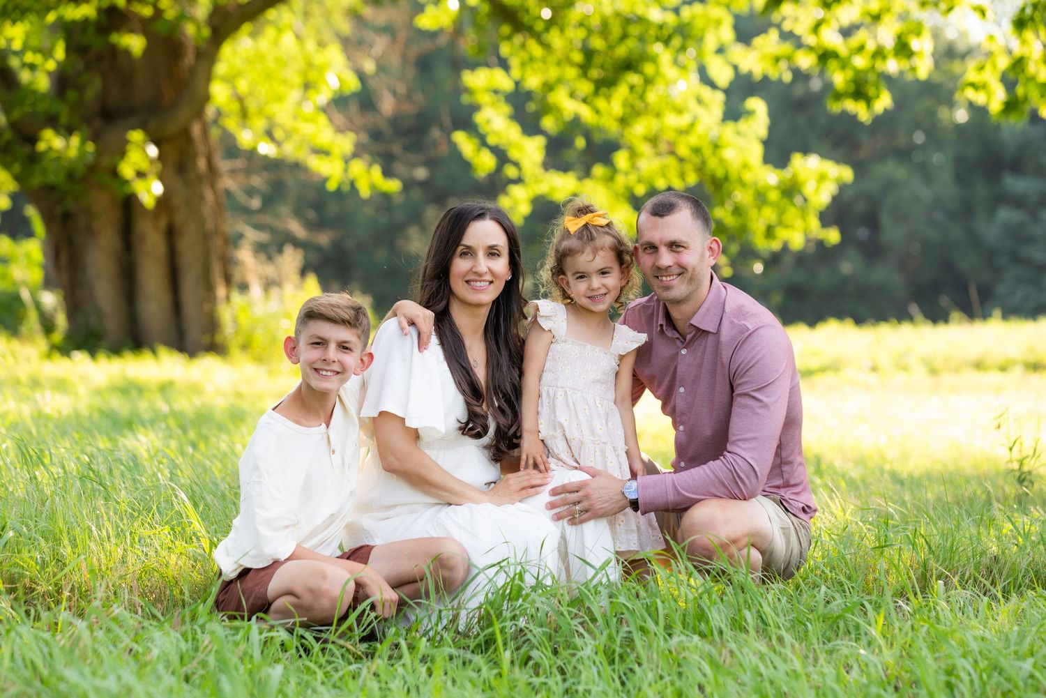 Family of five poses outdoors in front of lush green pine trees, including a baby held by parents.