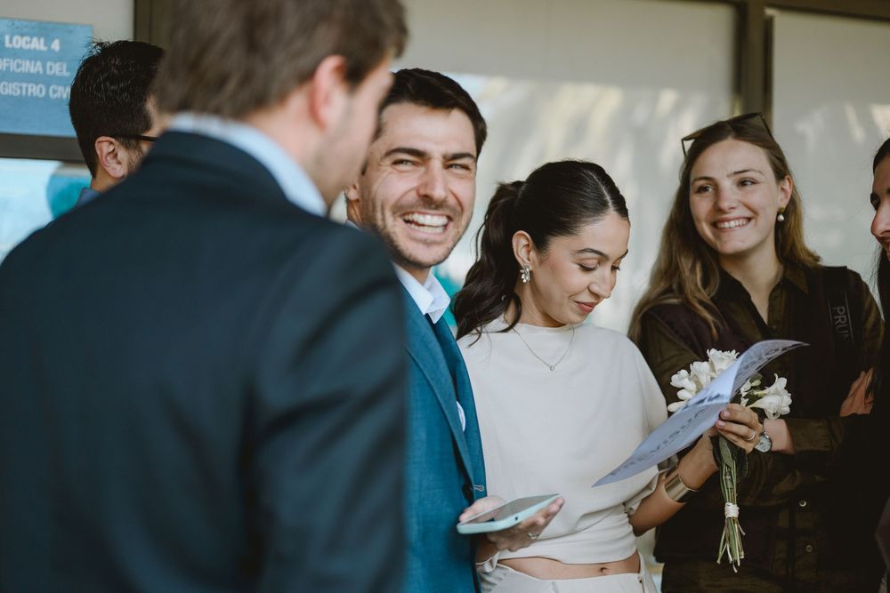 Smiling guests gather during a civil wedding ceremony, with the bride holding flowers and papers.