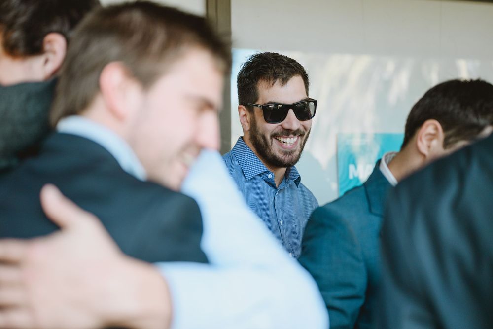 Smiling man in sunglasses and blue shirt socializing at an indoor wedding reception gathering.
