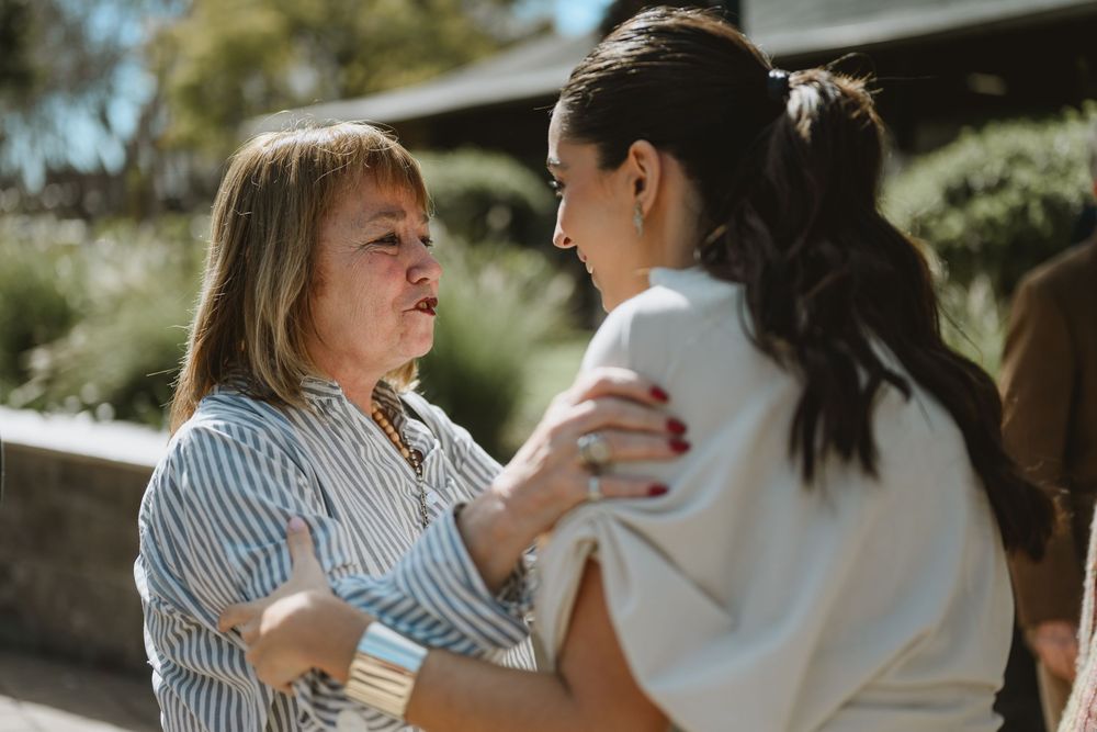 Two women share an emotional embrace outdoors, one consoling the other with a gentle touch on the shoulder.