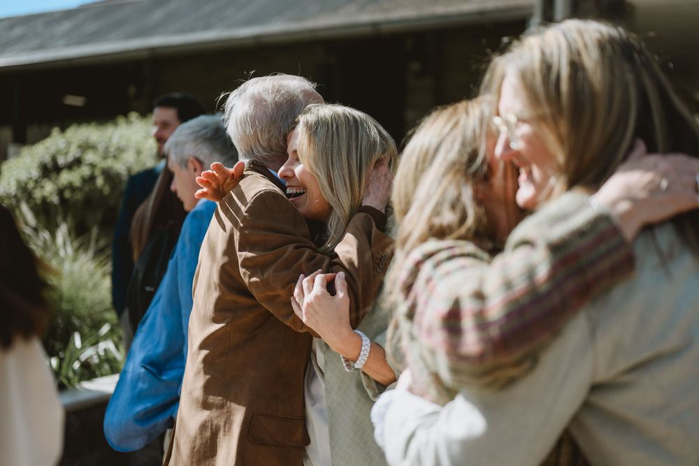 Groups of people sharing warm embraces outdoors near a building on a sunny day.