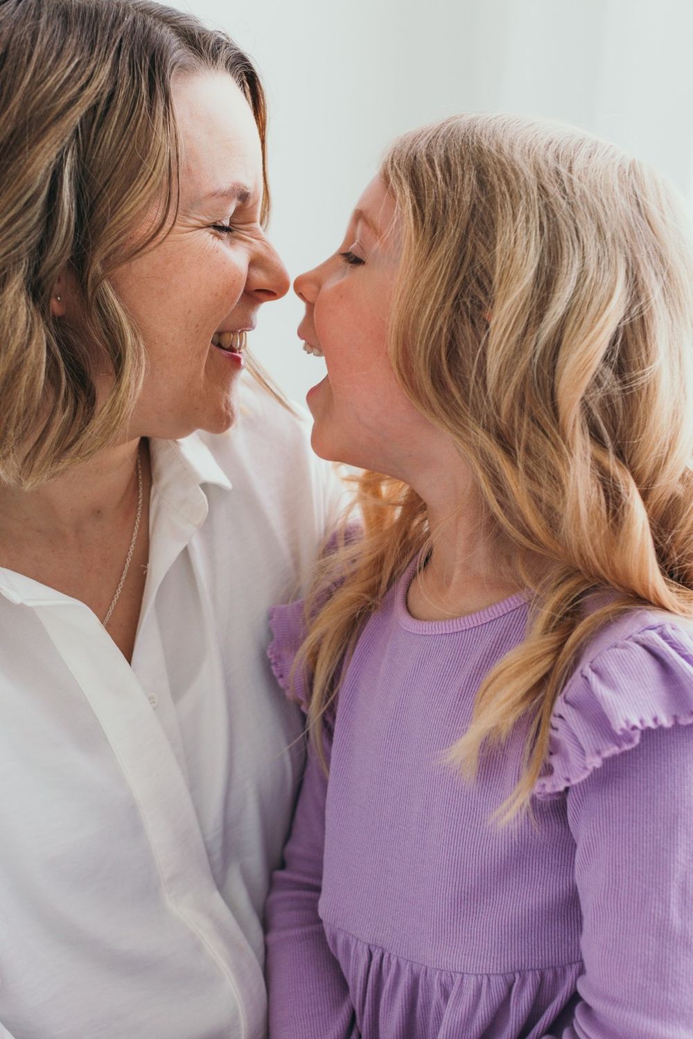 A woman and young girl touching noses and laughing together, sharing a joyful mother-daughter moment.