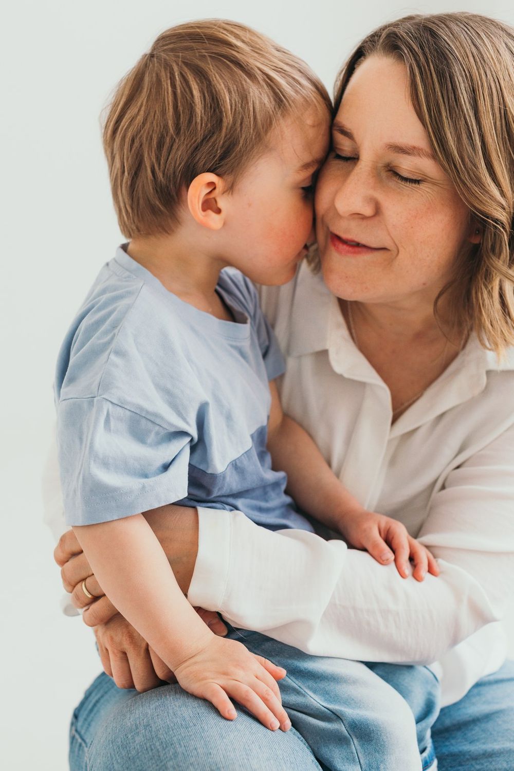 A tender moment between a mother and toddler son, with the child leaning his cheek against hers as she smiles warmly.