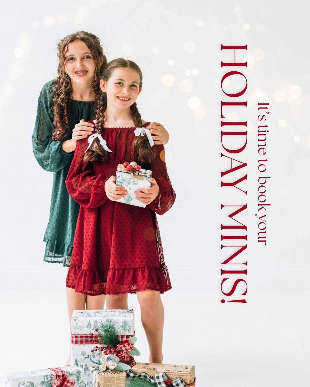 Two girls in festive red and green dresses pose with Christmas gifts for holiday mini photo sessions.