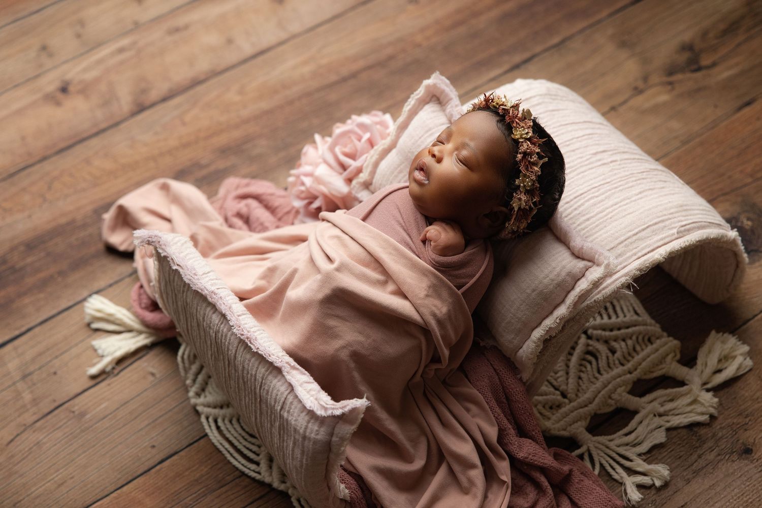 Newborn baby resting chin on hands inside a teal bucket with soft blanket, studio photography.
