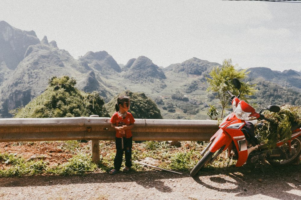 Solo traveler standing beside a red motorbike on a mountain road in rural Vietnam.