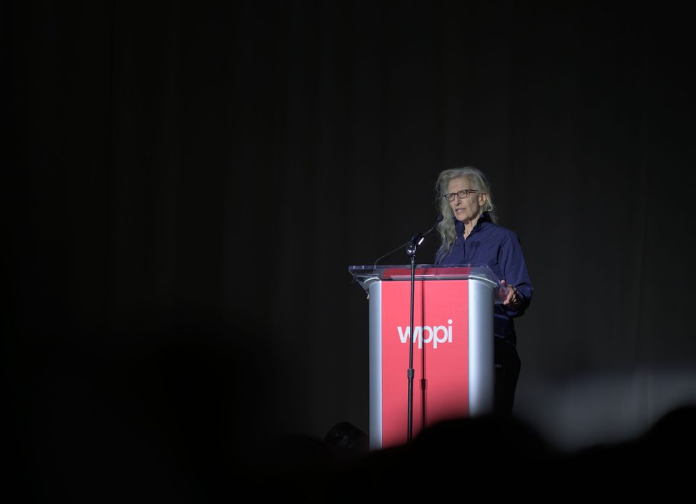 Speaker at a WPPI podium delivering a presentation on a dark stage.