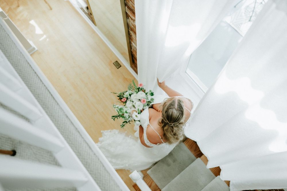 Aerial view of a bride in a white wedding gown holding a floral bouquet while descending a staircase.