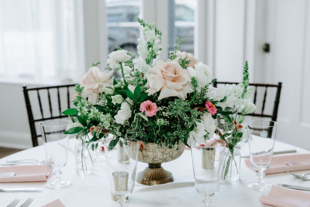 Elegant wedding centerpiece with white roses and greenery in a gold urn vase on a white tablecloth.