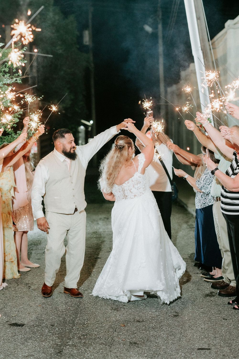 Bride and groom walk through sparkler exit tunnel at night during wedding reception celebration.