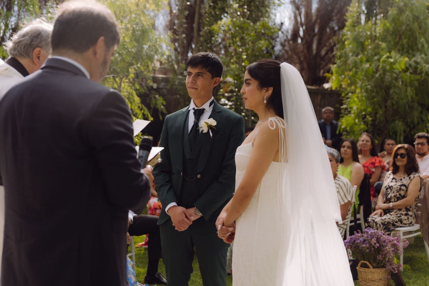 Bride and groom hold hands facing each other during intimate outdoor garden wedding ceremony.
