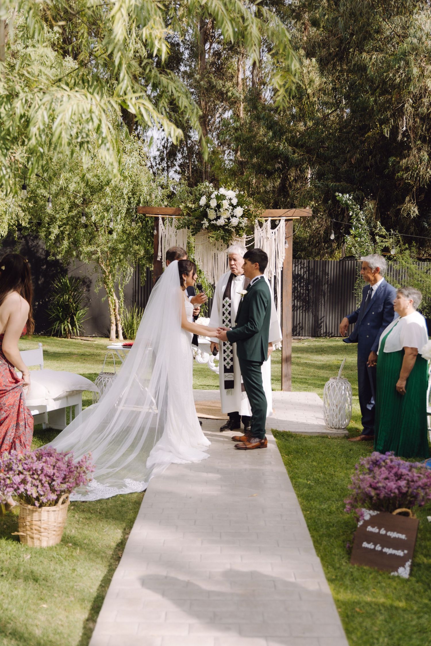 Bride and groom hold hands at floral altar during elegant outdoor garden wedding ceremony.