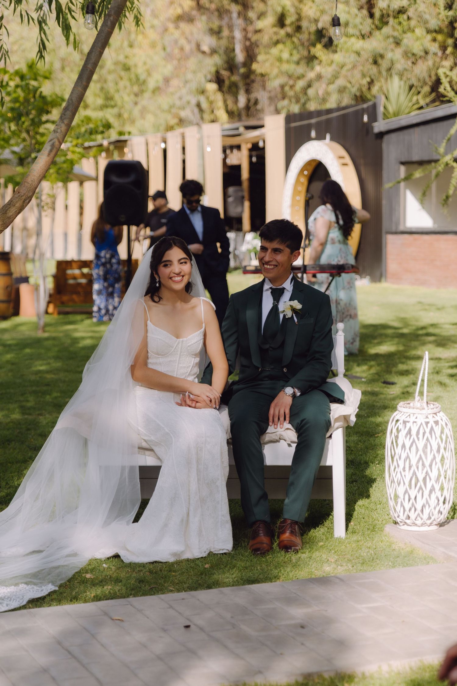 Happy bride and groom smile together while seated during elegant outdoor garden wedding ceremony.