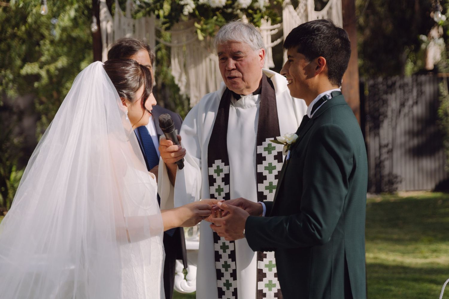 Officiant joins hands of bride and groom during outdoor garden wedding ring exchange ceremony.