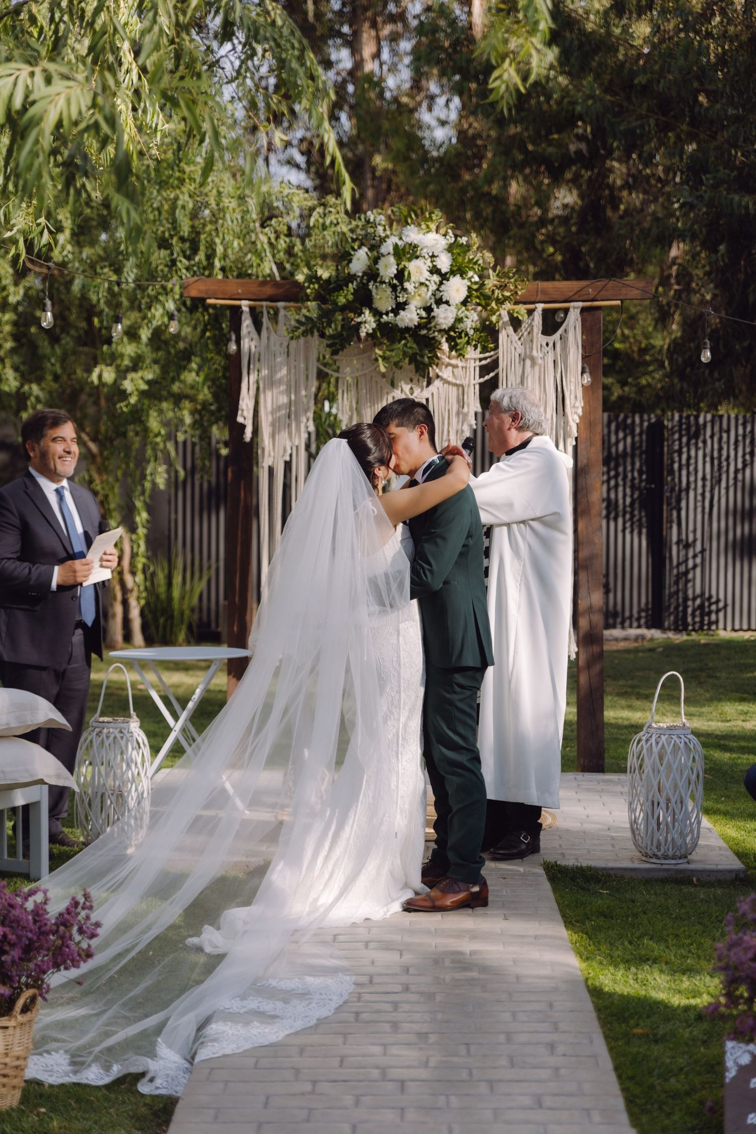 Bride and groom share first kiss under decorated floral arch at outdoor garden wedding.