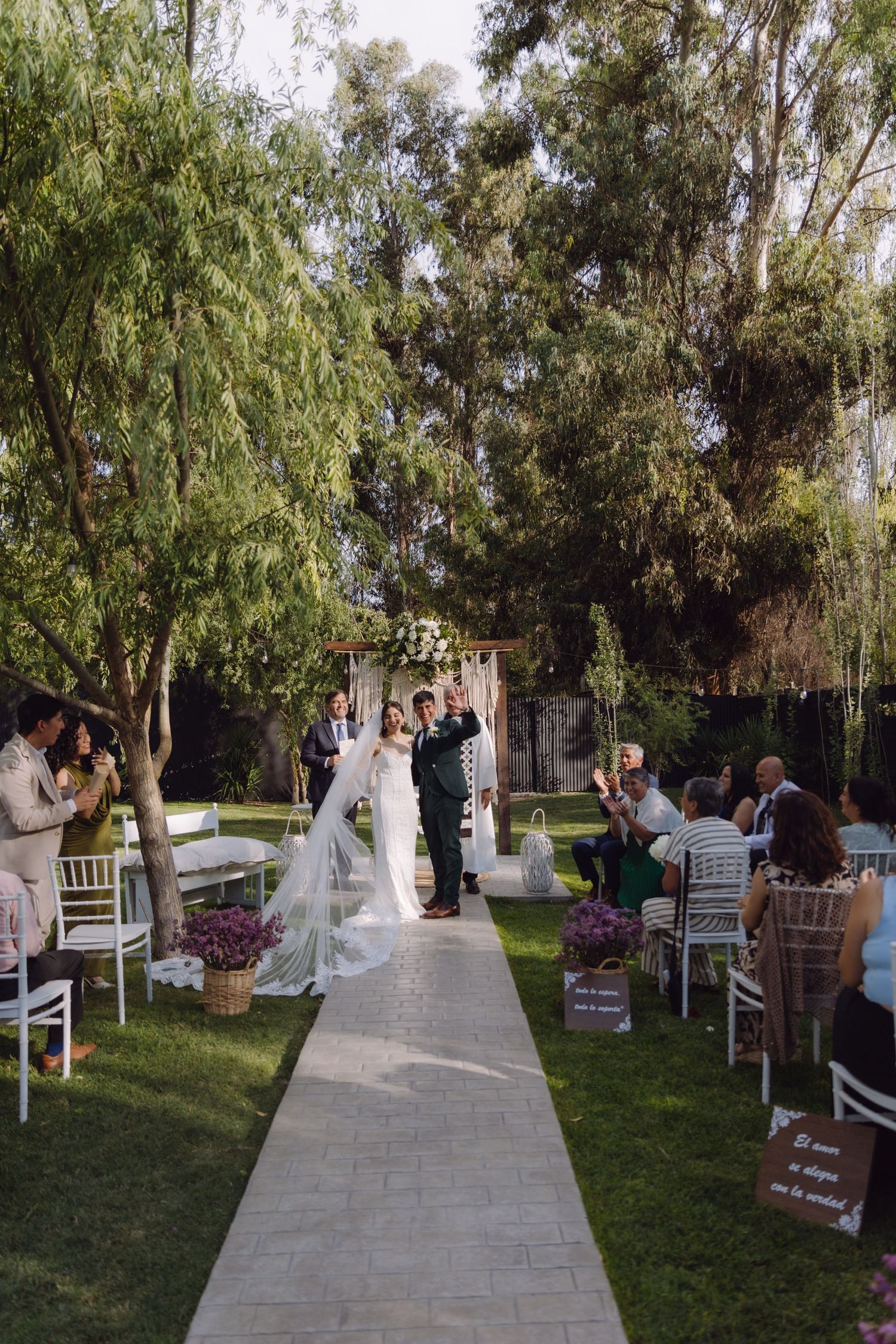 Newlywed couple walks down aisle surrounded by applauding guests at outdoor garden wedding.