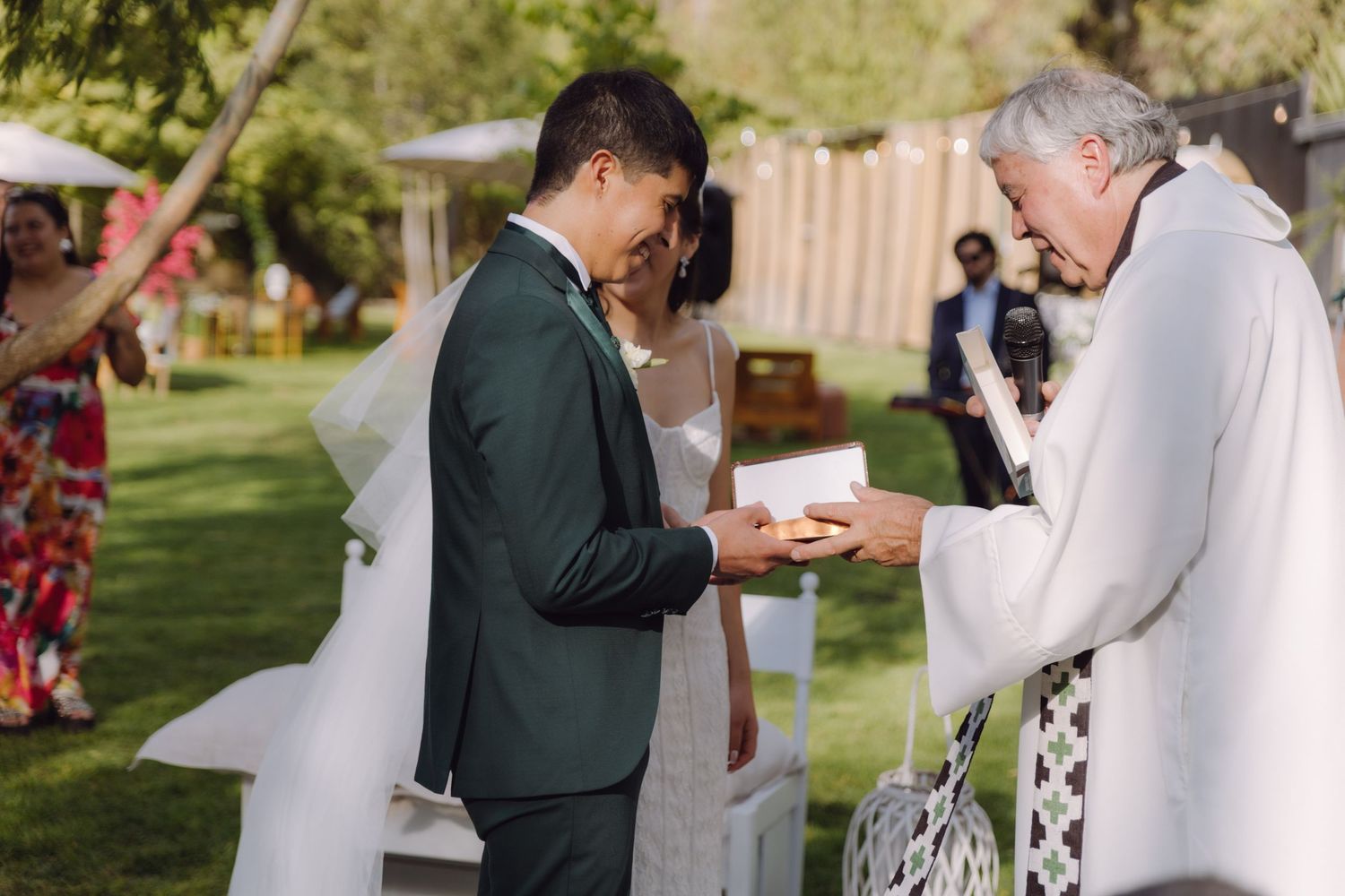 Groom receives wedding rings from officiant during outdoor garden wedding ceremony exchange.