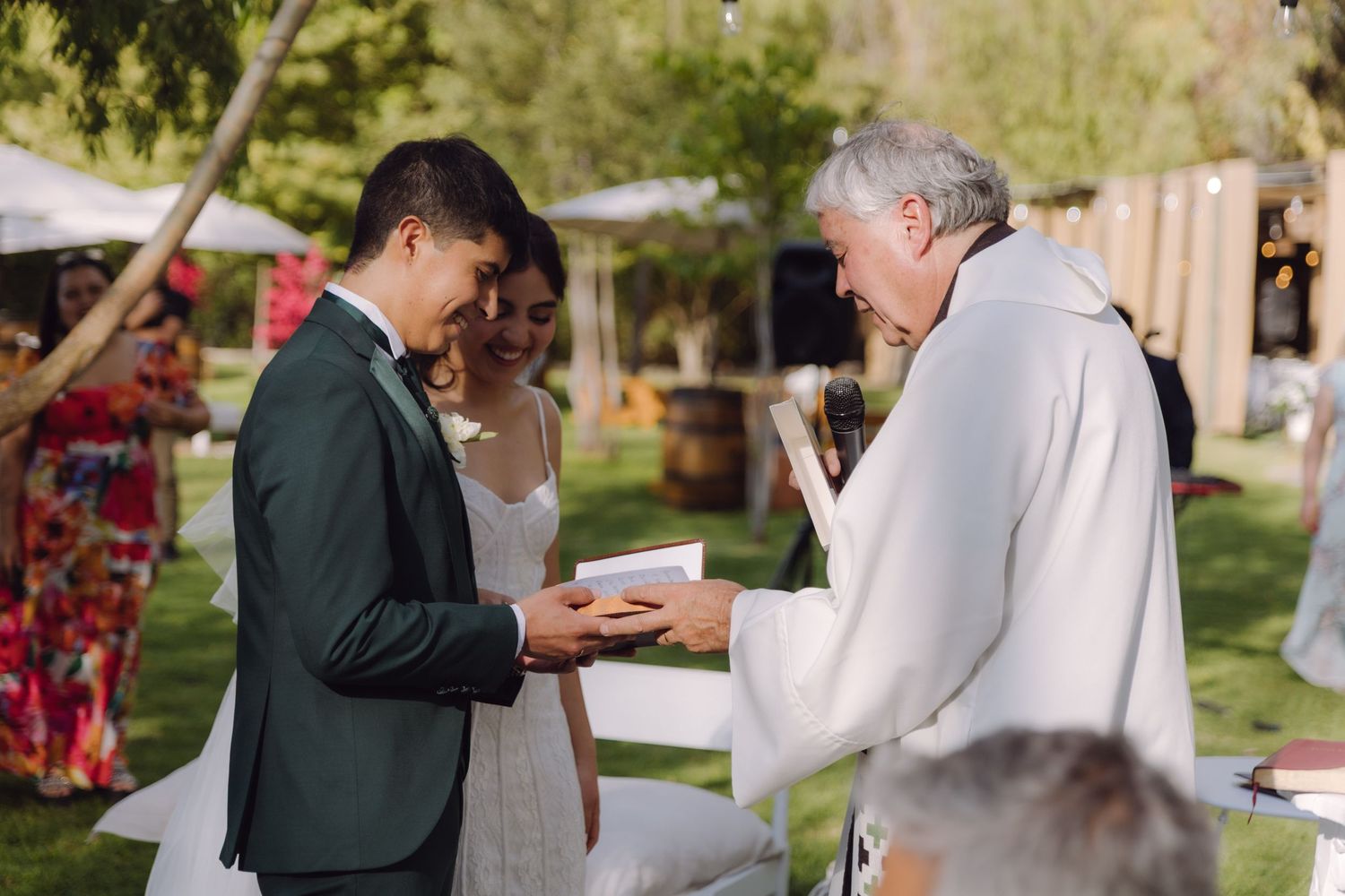 Groom receives wedding rings from officiant during outdoor garden ceremony.