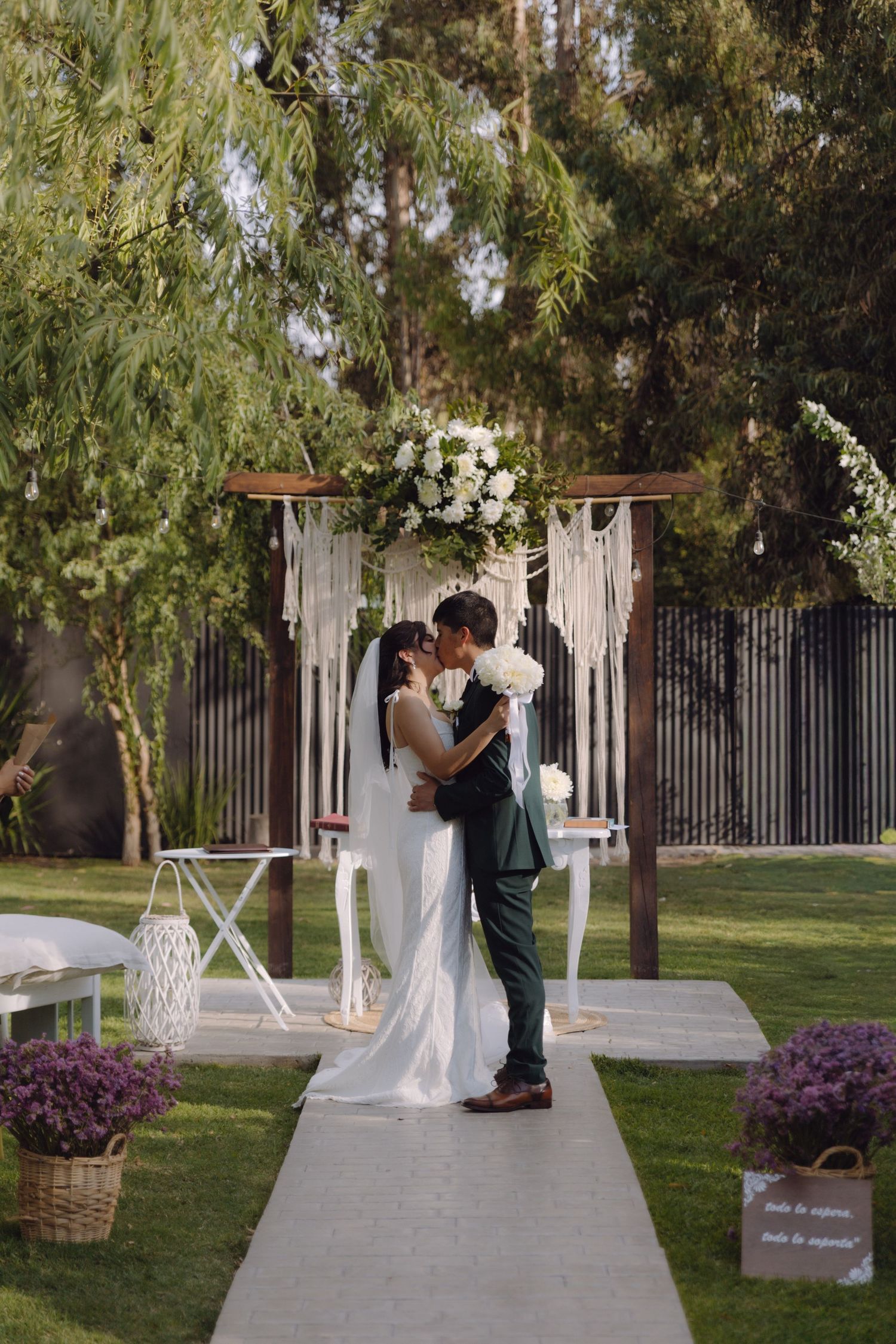 Bride and groom share first kiss at boho outdoor wedding altar with white florals.