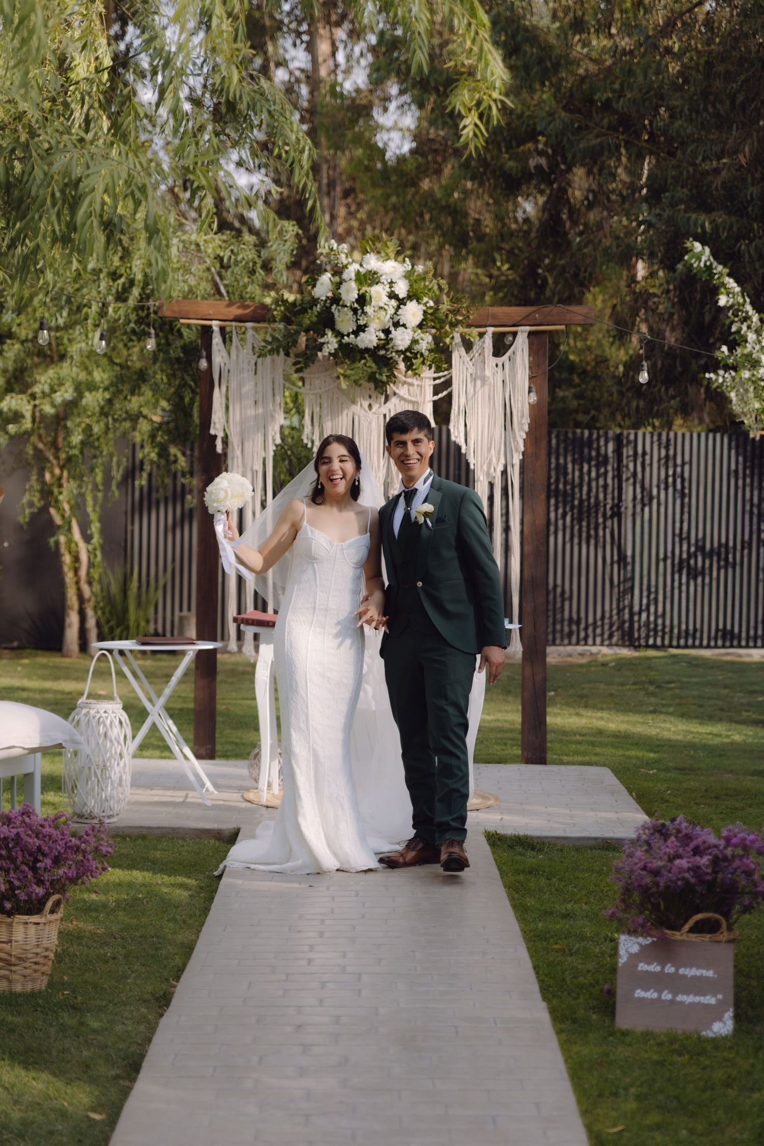 Happy bride and groom pose together at boho garden wedding altar after ceremony.