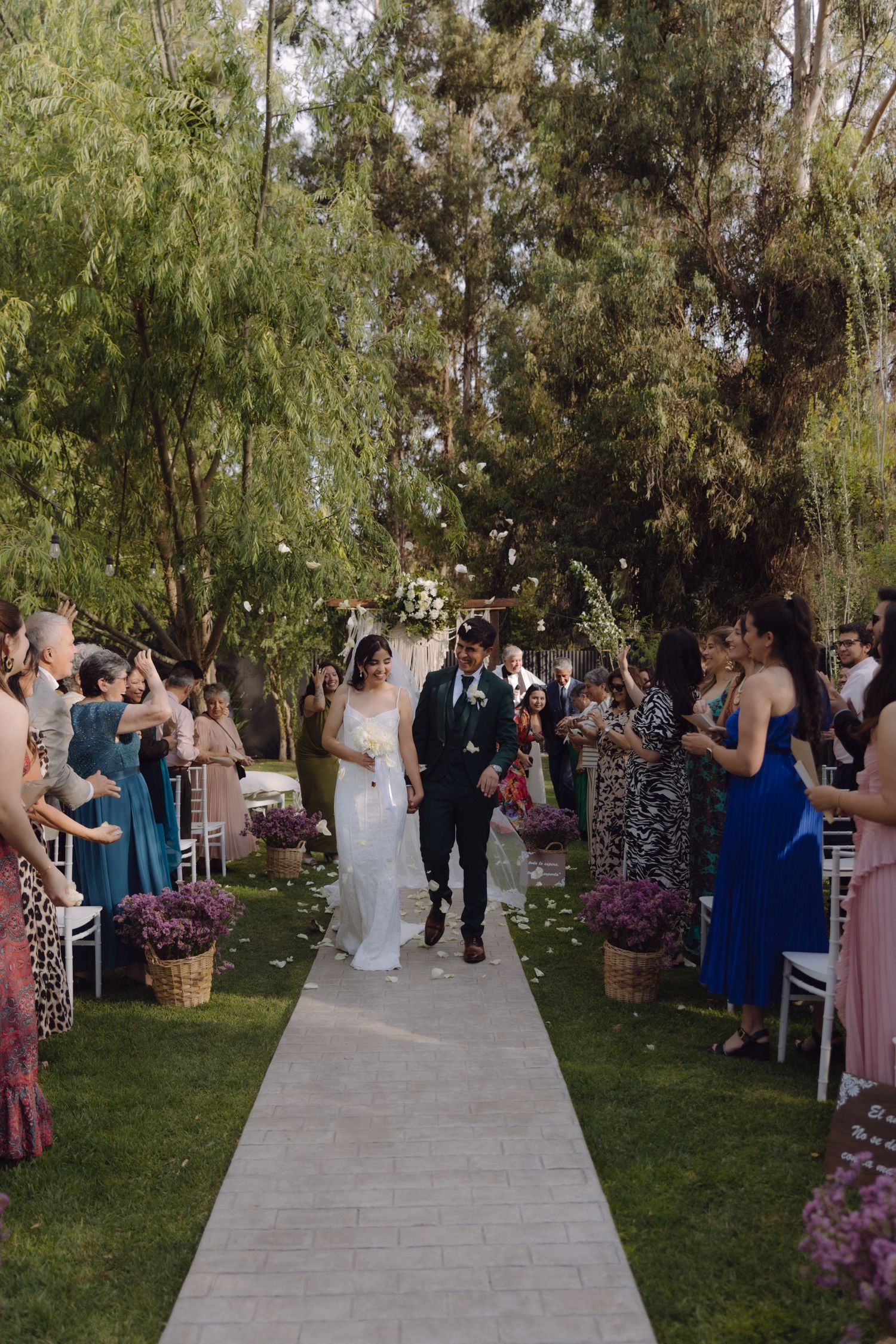 Bride and groom recess down aisle surrounded by cheering guests at garden wedding.