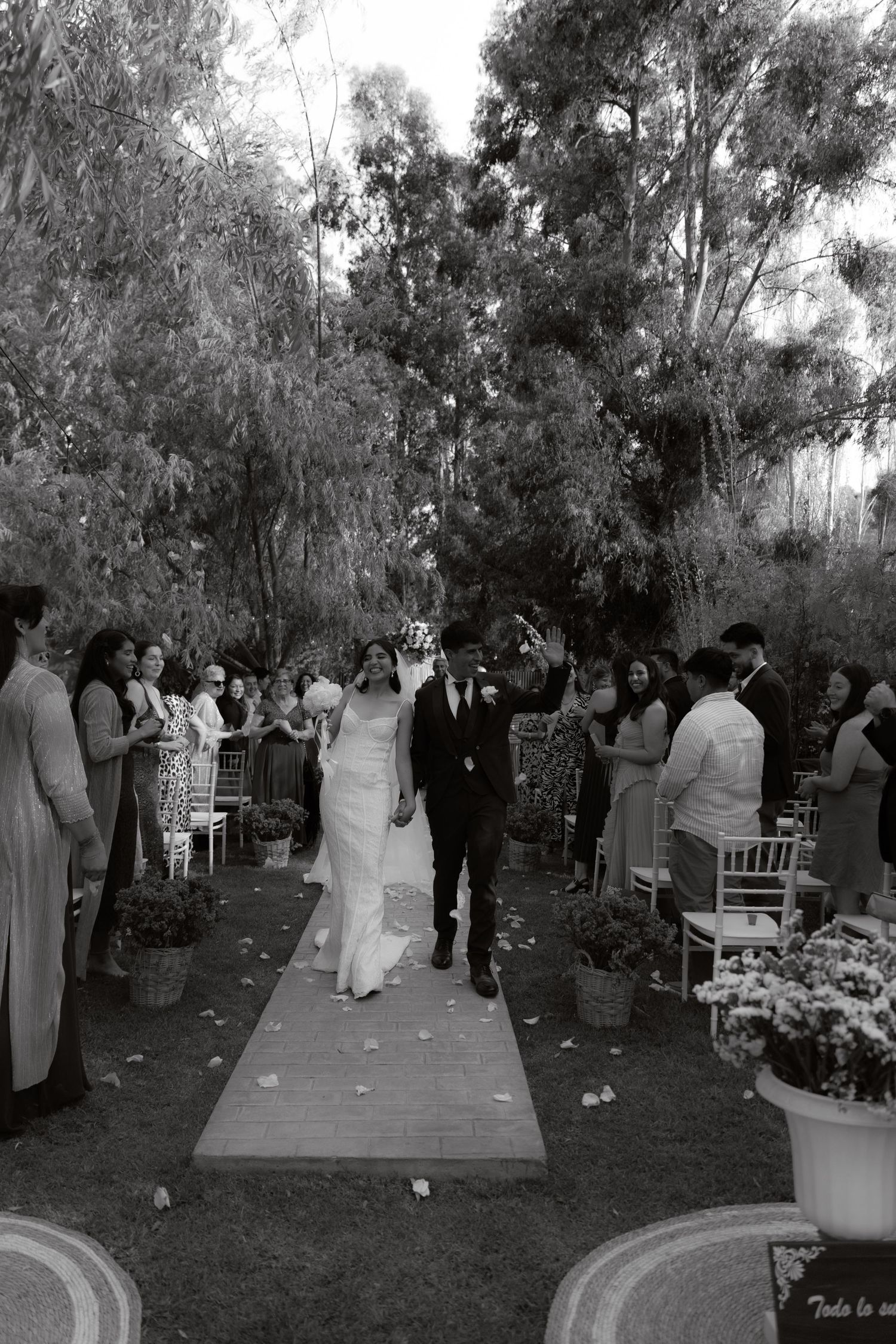 Black and white photo of joyful newlyweds recessing down aisle at outdoor garden wedding.