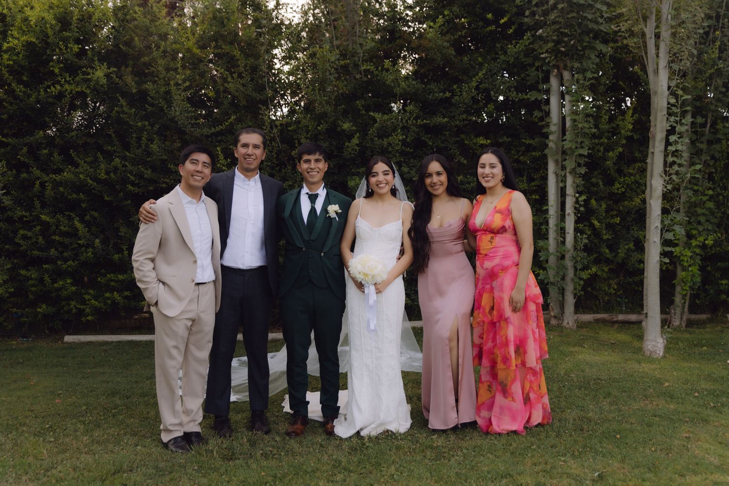 Wedding group photo with bride, groom, and four guests in pink and floral dresses.
