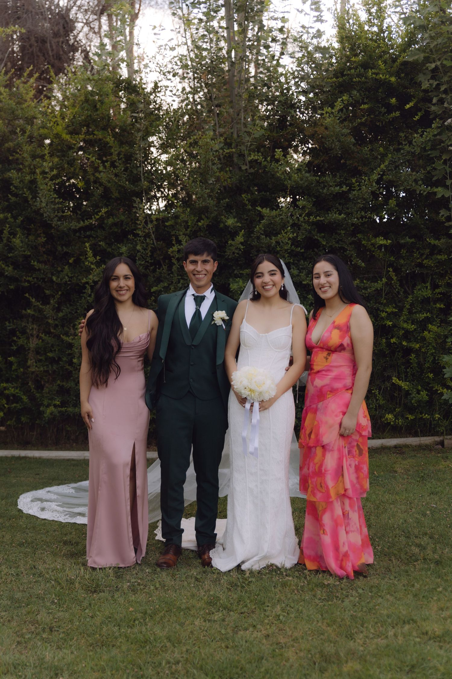 Bride and groom with two women in pink and floral dresses in garden.