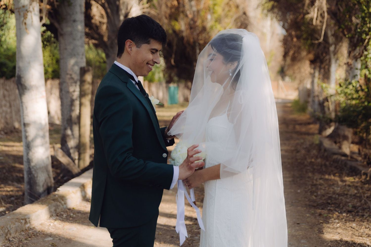 Bride and groom hold hands and smile at each other in a romantic outdoor wedding portrait.