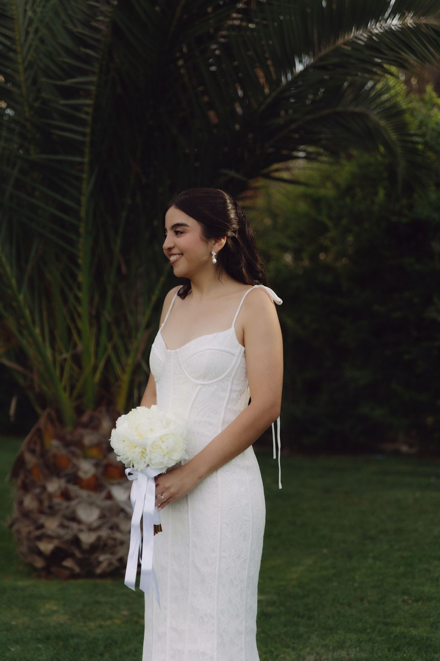 Smiling bride in white corset mermaid dress holds white hydrangea bouquet outdoors.