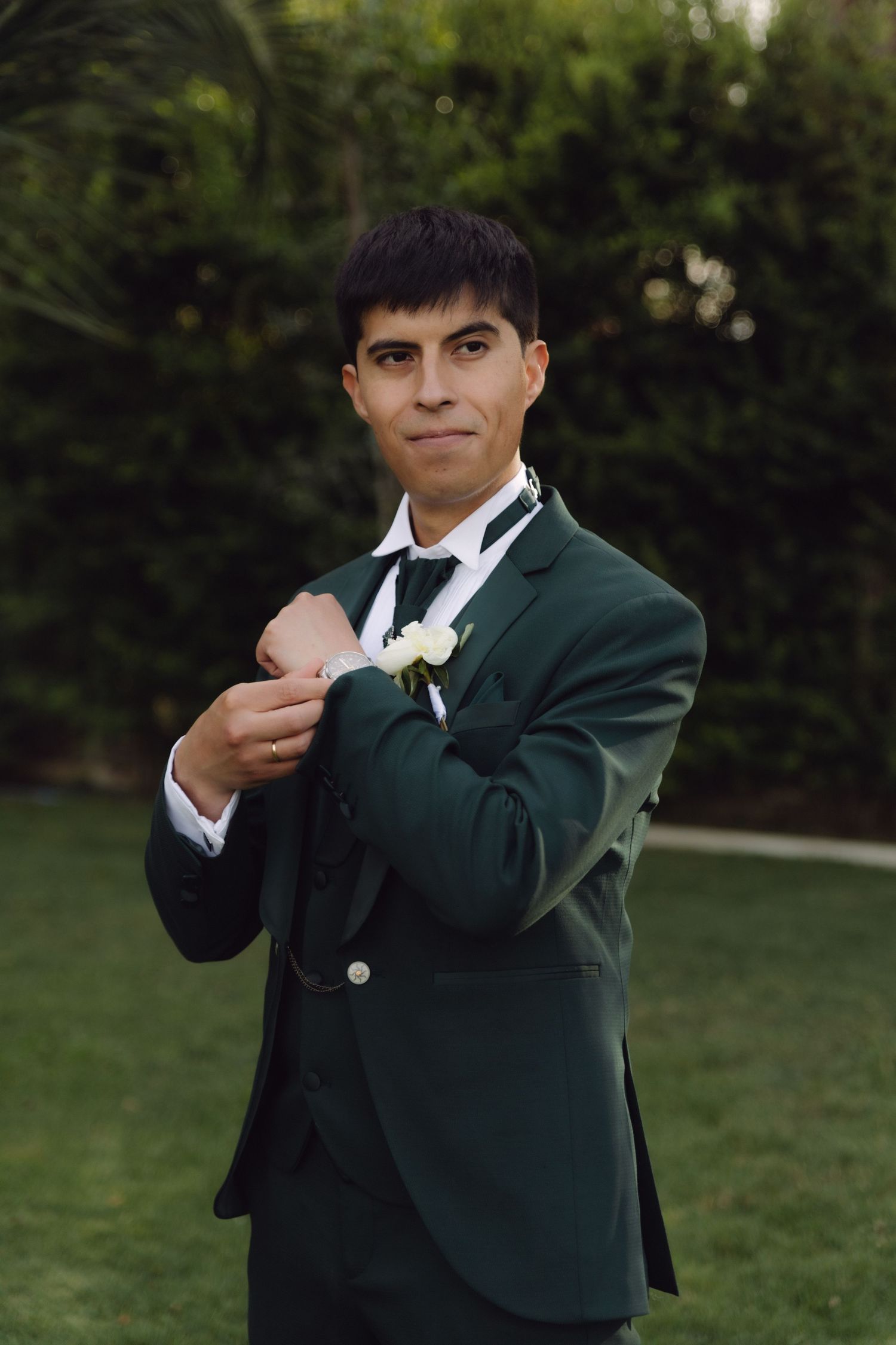 Dapper groom in emerald green suit adjusting cufflinks with white rose boutonniere.