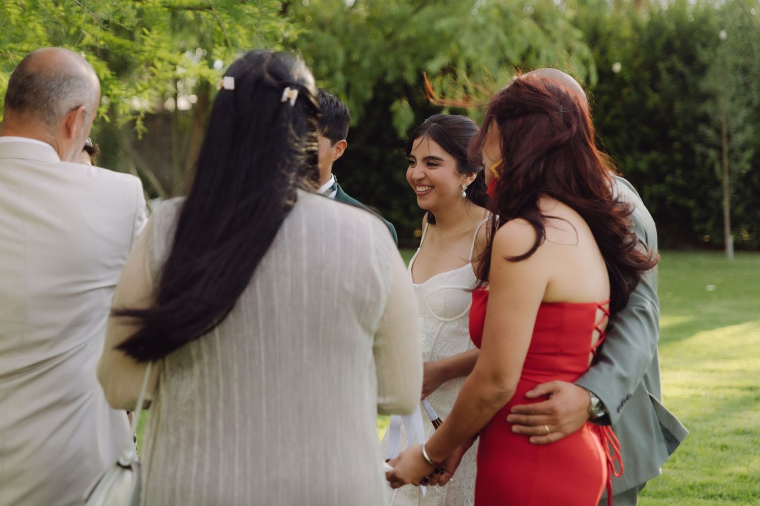 Bride in white dress smiling while greeting guests at outdoor wedding reception.