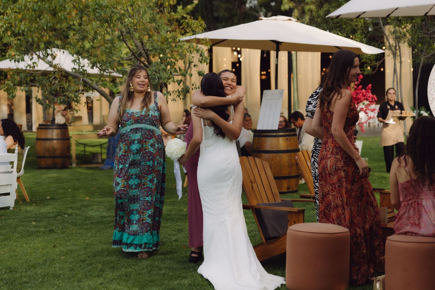 Bride in white mermaid dress embracing guest at elegant outdoor garden wedding reception.