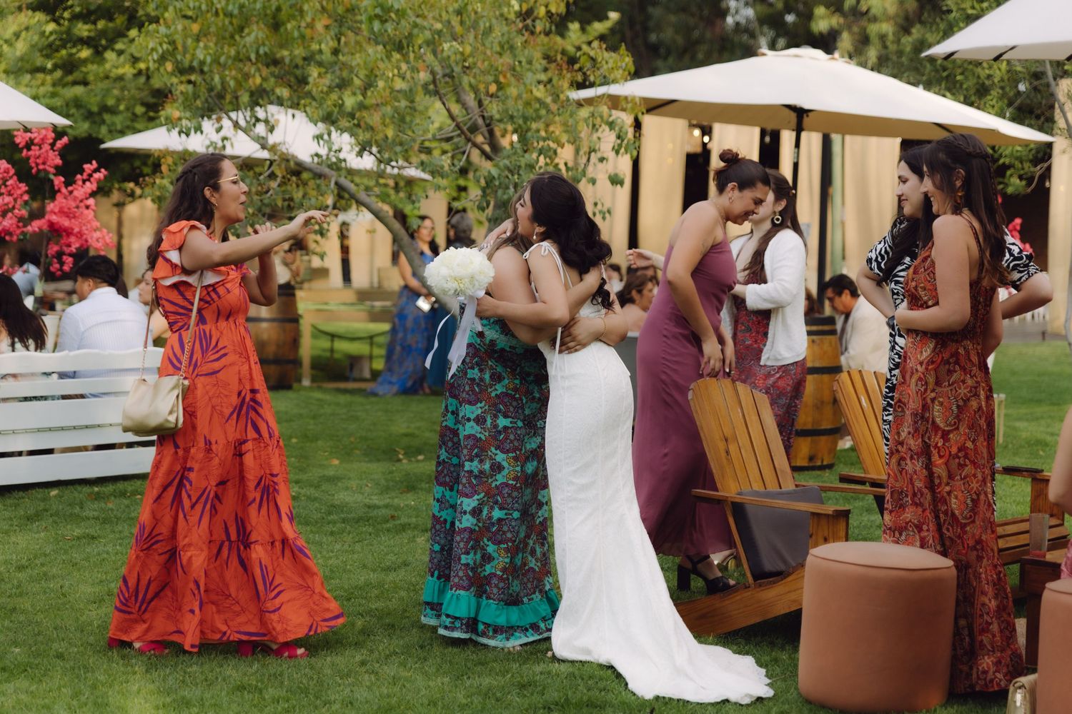 Bride in white gown greeted by colorfully dressed guests at outdoor garden wedding.