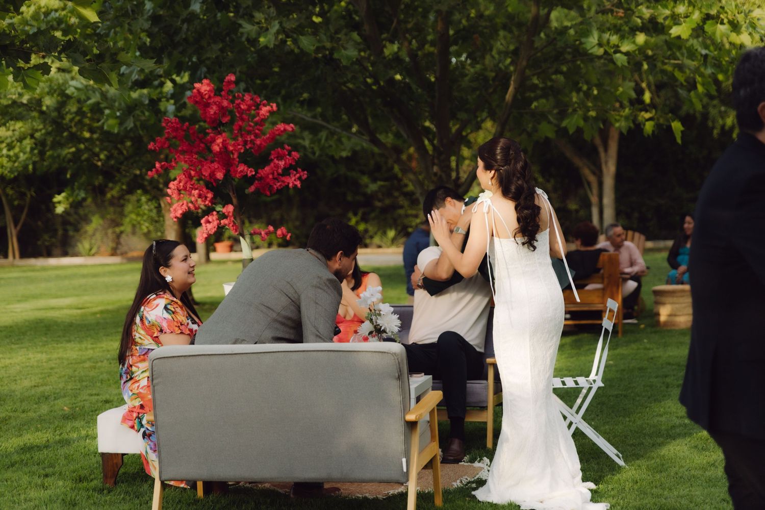 Bride in white wedding dress greeting seated guests at an elegant outdoor garden wedding reception.