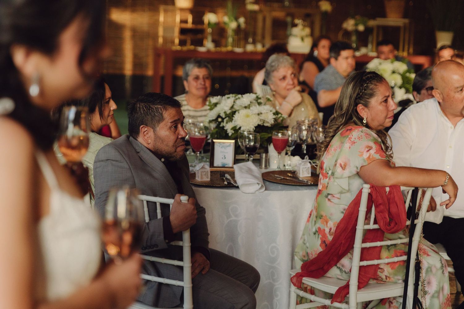 Wedding guests seated at elegantly decorated reception table with white floral centerpiece.