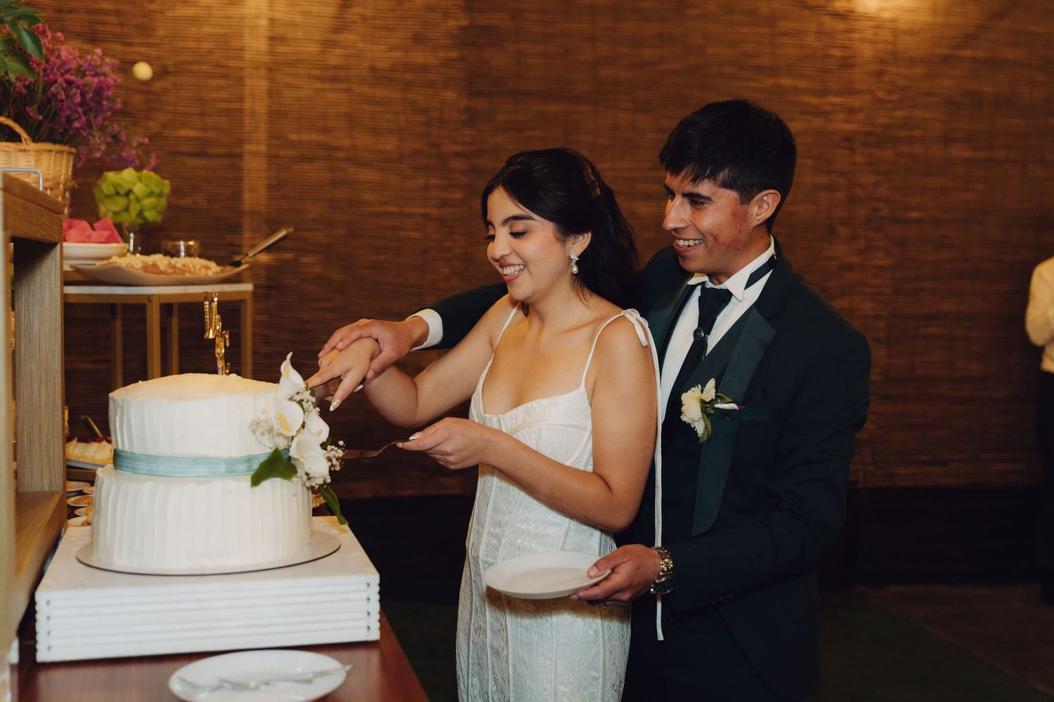 Bride and groom cutting elegant white tiered wedding cake with floral decoration at reception.