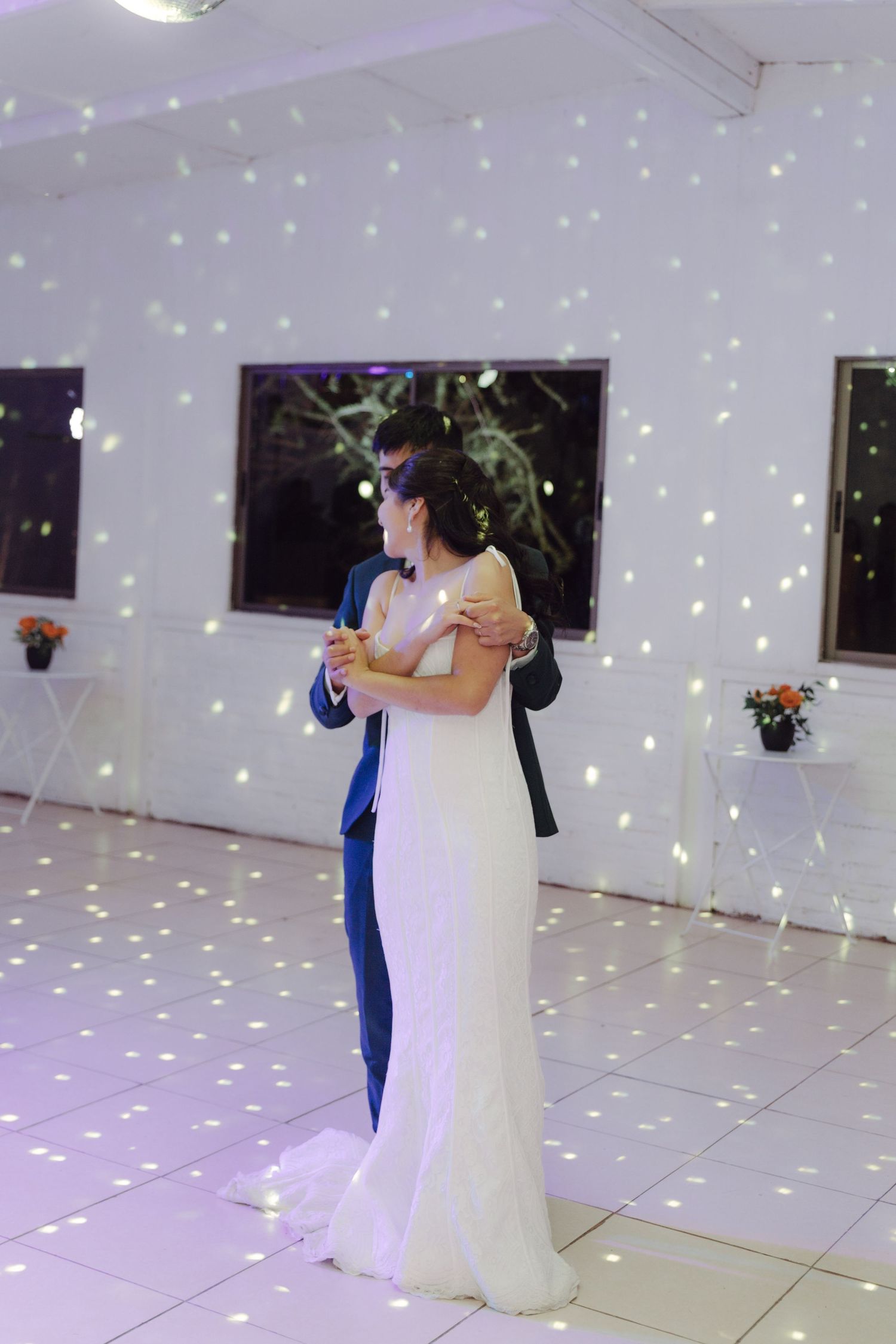 Bride and groom sharing romantic first dance on illuminated white dance floor at wedding reception.
