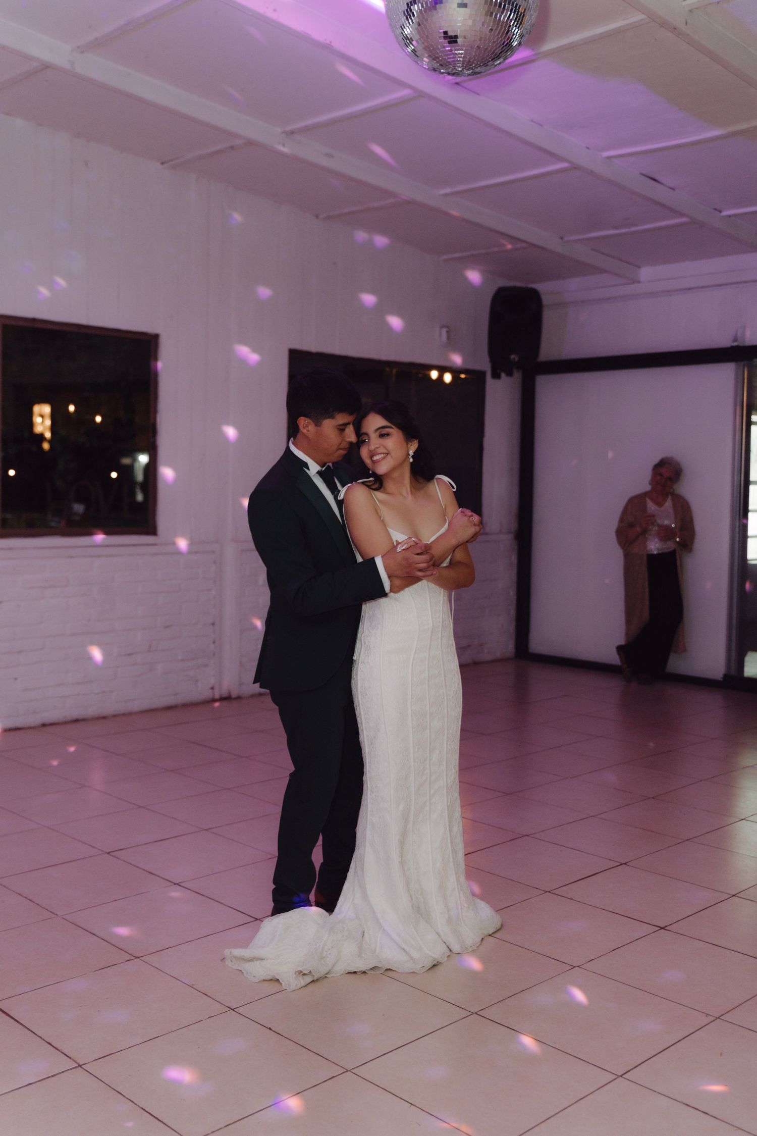 Bride and groom share their first dance under a disco ball in a softly lit wedding reception venue.