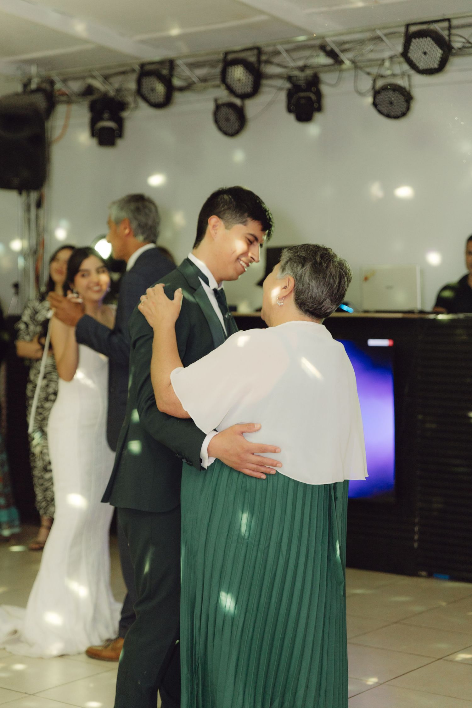 Groom dancing with his mother in a green dress during a wedding reception.
