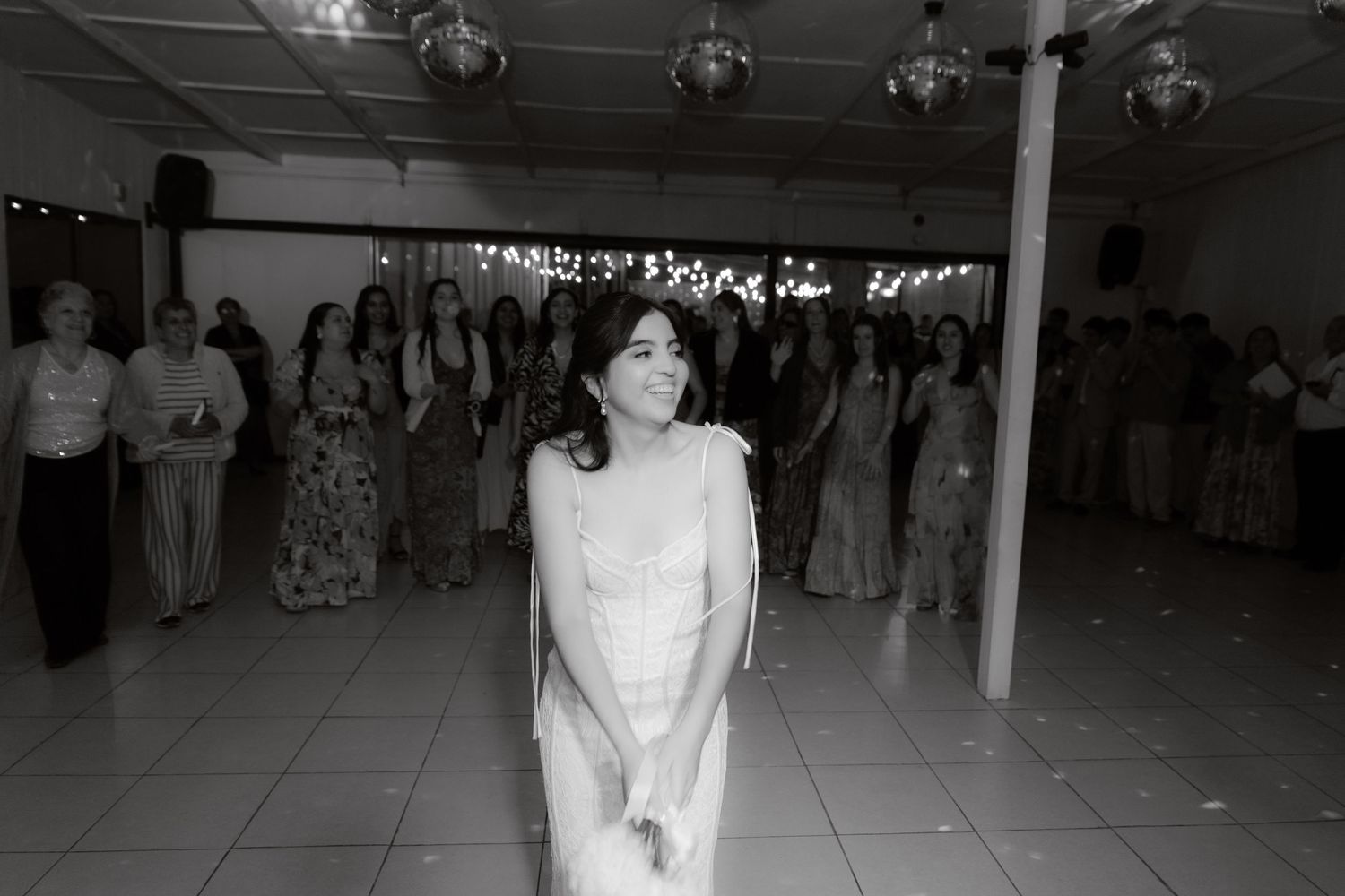 Bride in white gown preparing to toss the bouquet at wedding reception, black and white photo.