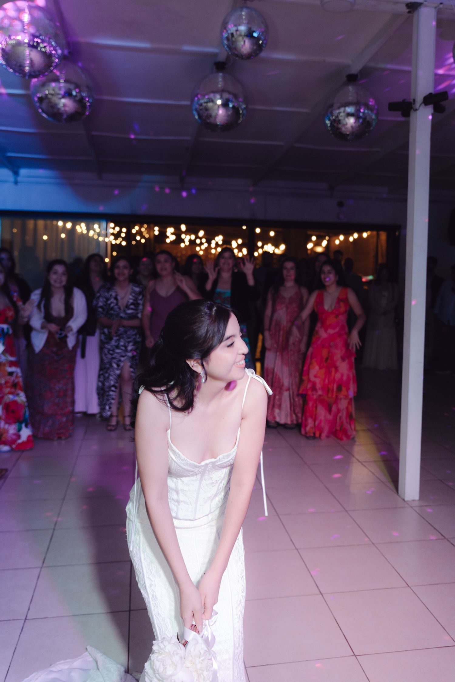 Bride in white dress about to throw the bouquet to guests at a colorful wedding reception.